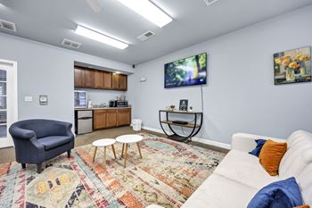A living room with a white couch, a blue armchair, and a rug with a pattern at Peachtree Place Apartments, Columbia, SC
